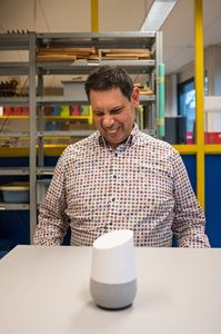 Foto van lachende man, bewoner van Visio wonen met een Google Home speaker.